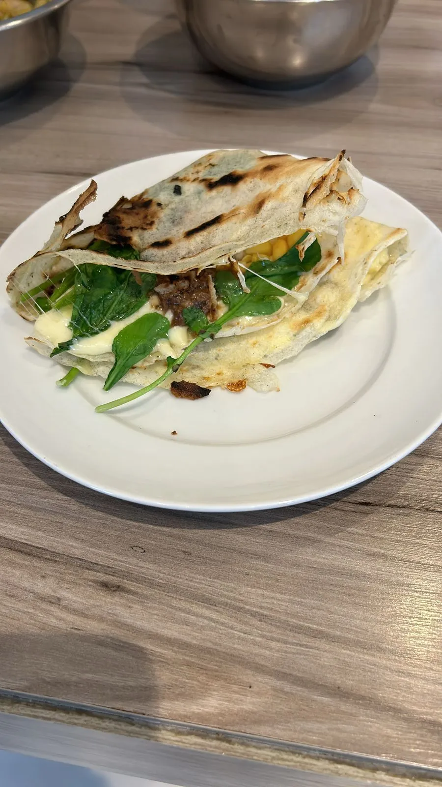 Grilled folded flatbread sandwich with melted cheese, spinach, and meat on a white plate.